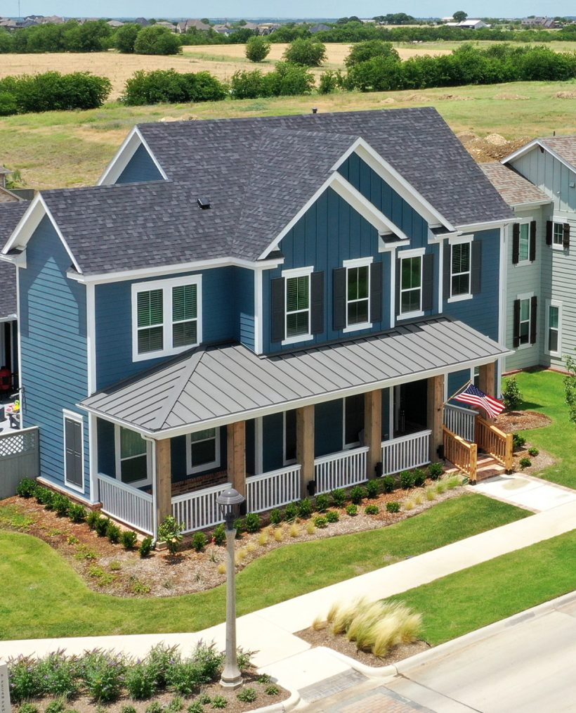 aerial of 2-story blue gray home with white fence around front porch