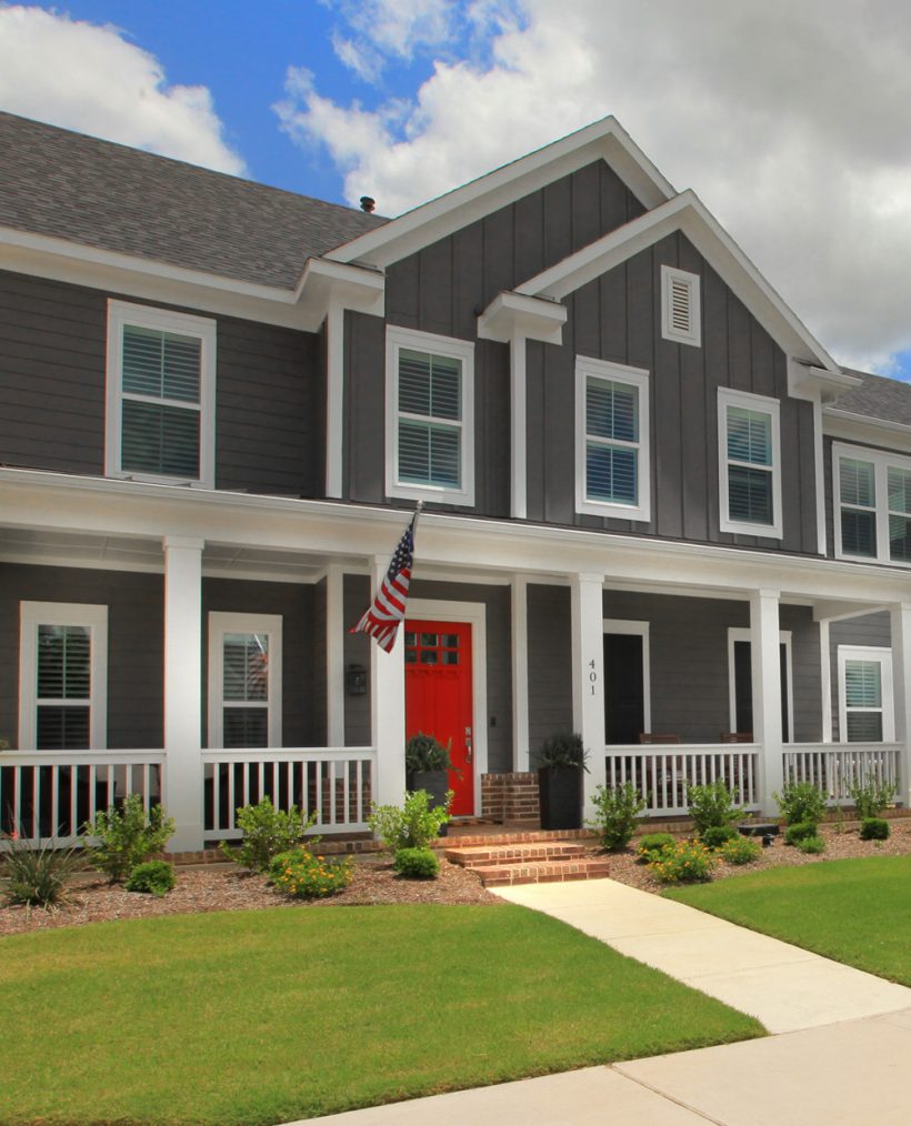 2-story dark gray home with red door and white fence around front porch